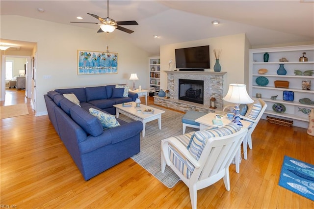 living area featuring built in features, a ceiling fan, light wood-style flooring, vaulted ceiling, and a stone fireplace