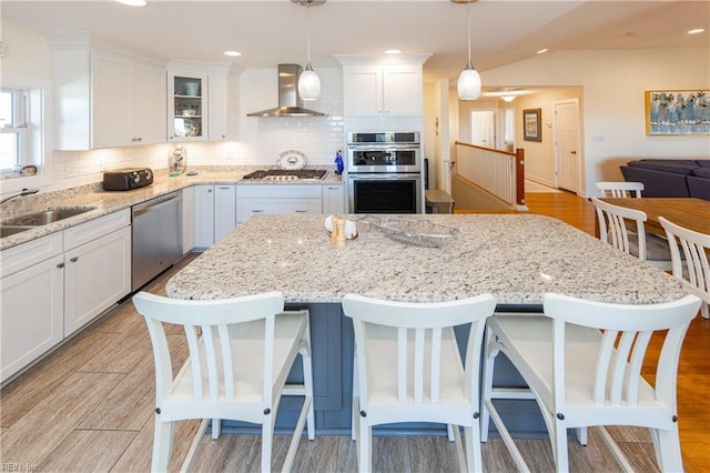 kitchen with wall chimney exhaust hood, white cabinetry, stainless steel appliances, and a sink