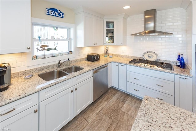 kitchen with tasteful backsplash, white cabinets, wall chimney exhaust hood, stainless steel appliances, and a sink