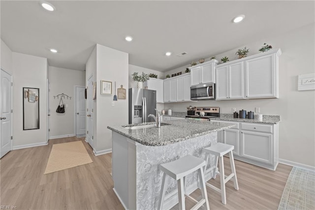 kitchen with stainless steel appliances, light wood-style floors, white cabinetry, and a sink