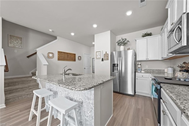 kitchen featuring stainless steel appliances, visible vents, white cabinets, a sink, and light stone countertops