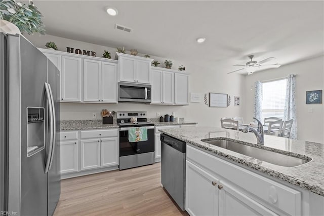 kitchen with stainless steel appliances, a sink, white cabinetry, a ceiling fan, and light wood finished floors