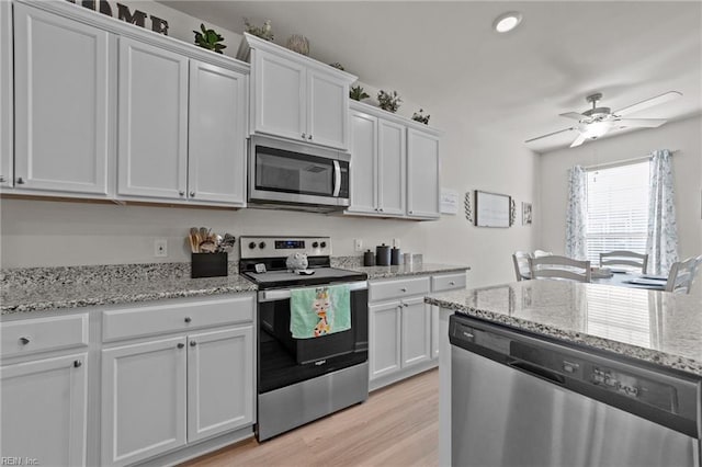 kitchen featuring stainless steel appliances, white cabinets, ceiling fan, light stone countertops, and light wood-type flooring