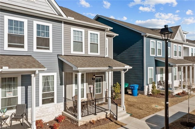 multi unit property featuring a porch, stone siding, and a shingled roof