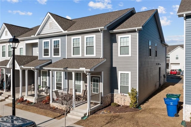 townhome / multi-family property featuring stone siding, a residential view, a porch, and roof with shingles