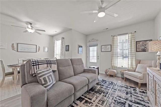 living area with light wood-style flooring, visible vents, baseboards, and ceiling fan