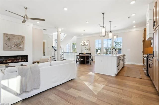 living area featuring recessed lighting, ceiling fan with notable chandelier, baseboards, light wood-style floors, and a glass covered fireplace