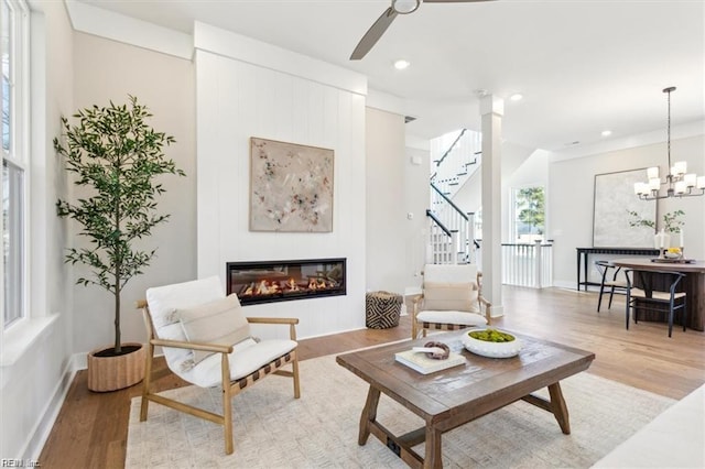 living area featuring stairway, a glass covered fireplace, a notable chandelier, and light wood-style flooring