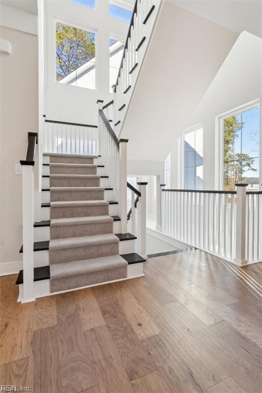 stairway with a healthy amount of sunlight, a towering ceiling, and wood finished floors