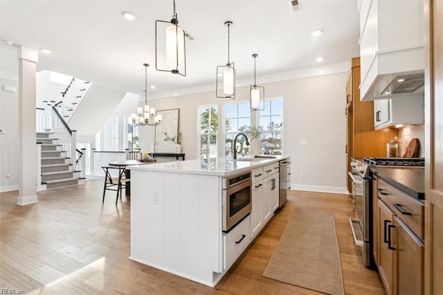 kitchen with an island with sink, custom range hood, a sink, stainless steel appliances, and backsplash