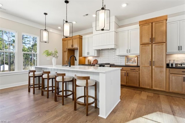 kitchen featuring wood finished floors, a sink, visible vents, tasteful backsplash, and a center island with sink