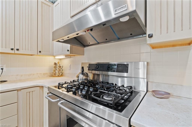 kitchen with under cabinet range hood, stainless steel gas range oven, and tasteful backsplash