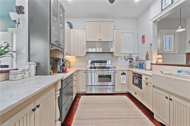 kitchen with under cabinet range hood, cream cabinets, range with two ovens, and dark wood-type flooring