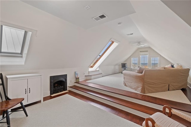 interior space with a fireplace with flush hearth, vaulted ceiling with skylight, visible vents, and wood finished floors