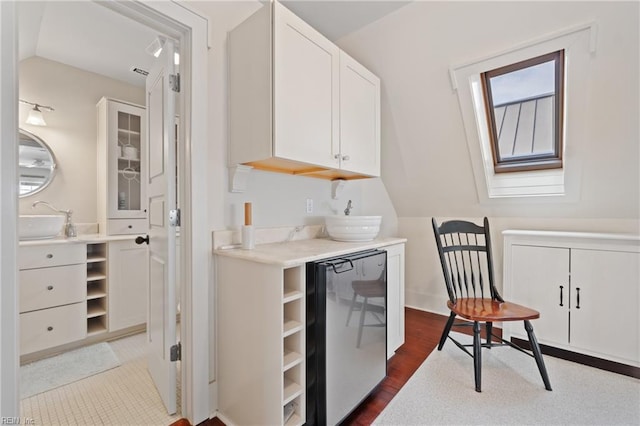 kitchen featuring vaulted ceiling with skylight, a sink, white cabinets, light countertops, and fridge