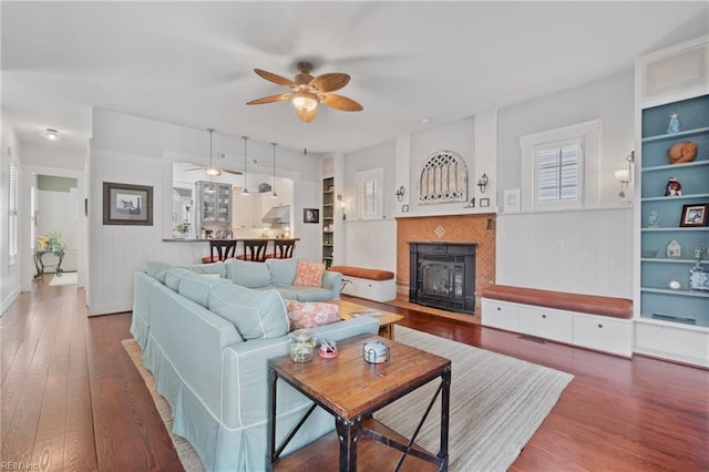 living room with ceiling fan, built in shelves, a tile fireplace, and wood finished floors