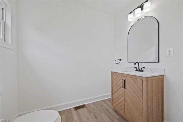 half bath with visible vents, toilet, wood finished floors, baseboards, and vanity