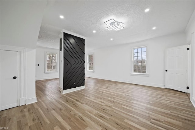 unfurnished living room with recessed lighting, light wood-type flooring, baseboards, and a textured ceiling