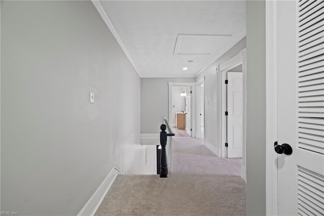 hallway featuring carpet, baseboards, attic access, ornamental molding, and an upstairs landing