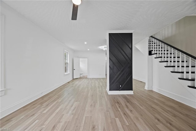 unfurnished living room with stairway, baseboards, a textured ceiling, and wood finished floors