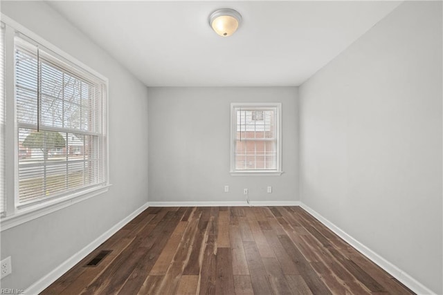 spare room featuring dark wood-style floors, visible vents, and baseboards