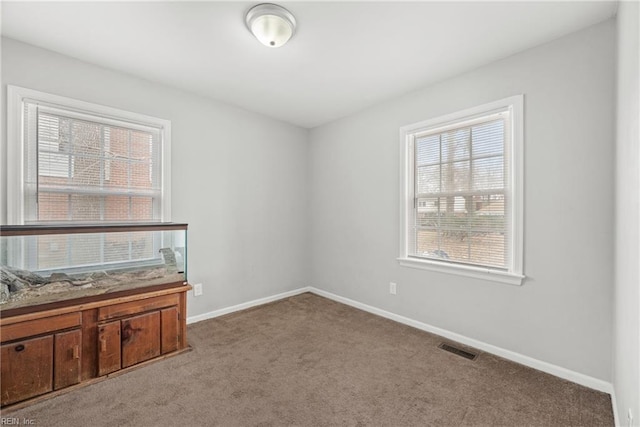 carpeted empty room featuring a wealth of natural light, visible vents, and baseboards