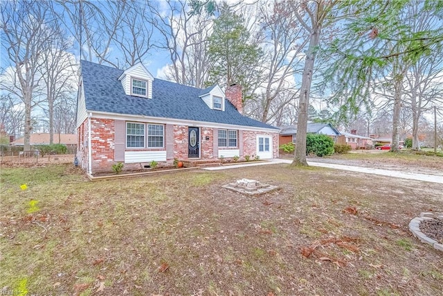 cape cod-style house featuring a front yard, a chimney, brick siding, and a shingled roof