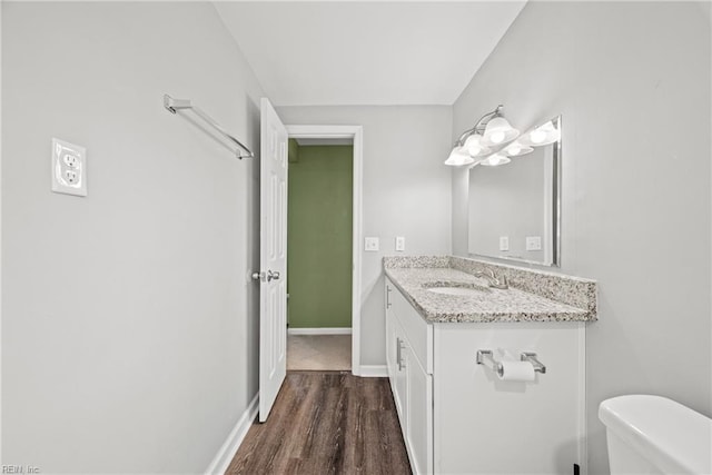 half bath featuring baseboards, toilet, wood finished floors, and vanity