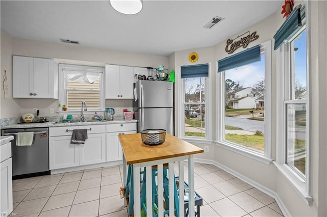 kitchen with appliances with stainless steel finishes, white cabinets, light tile patterned flooring, and a sink