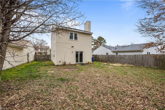 back of property featuring a lawn, a chimney, and a fenced backyard