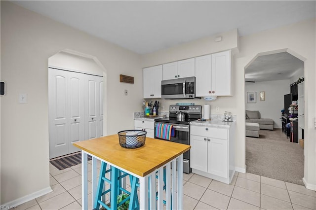 kitchen with arched walkways, light tile patterned floors, baseboards, white cabinets, and appliances with stainless steel finishes