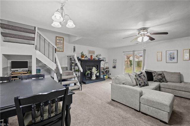 living room featuring stairs, ceiling fan with notable chandelier, a fireplace, and carpet flooring