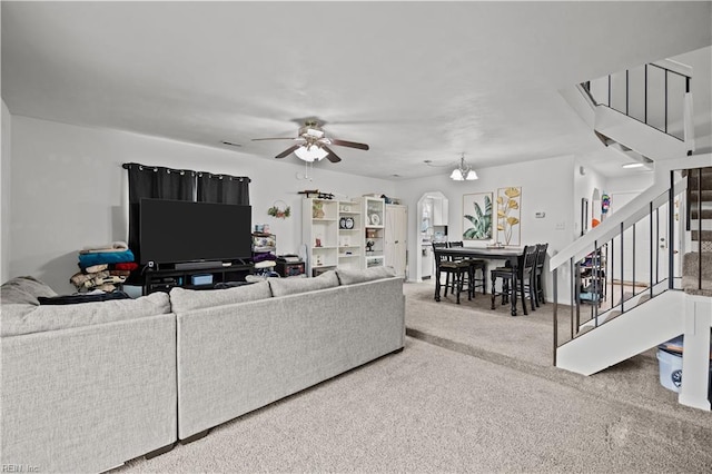 carpeted living room with stairway, arched walkways, and a ceiling fan