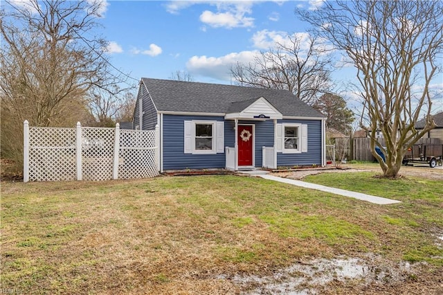 view of front of home with a front lawn, roof with shingles, and fence