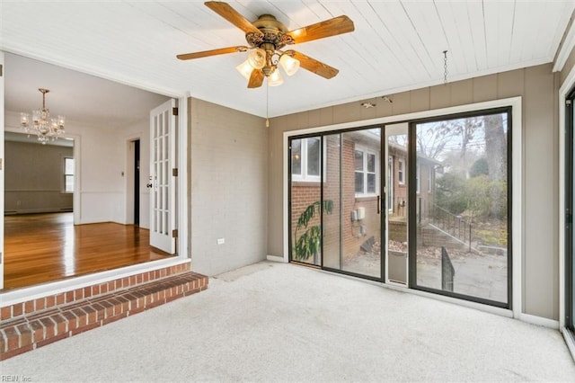 carpeted spare room featuring ceiling fan with notable chandelier and brick wall