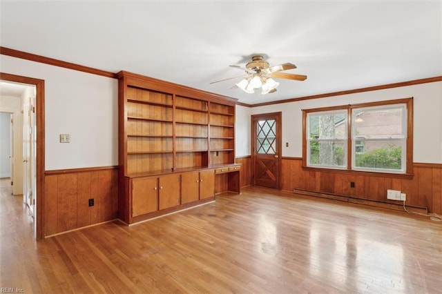 empty room featuring ceiling fan, a wainscoted wall, wood walls, light wood-style floors, and crown molding