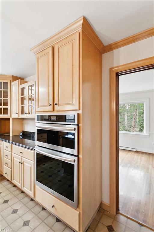 kitchen with a baseboard radiator, light brown cabinetry, double oven, glass insert cabinets, and ornamental molding