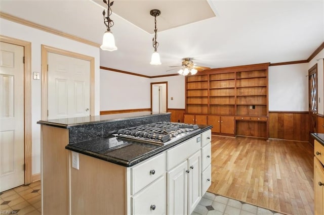 kitchen featuring a wainscoted wall, white cabinets, stainless steel gas stovetop, a center island, and crown molding