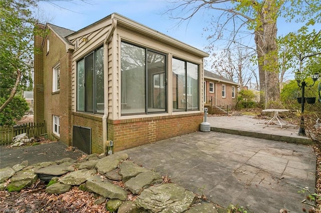 view of home's exterior with a sunroom, brick siding, fence, and a patio