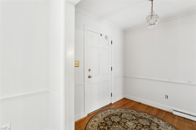 entryway with a baseboard heating unit, ornamental molding, an inviting chandelier, and wood finished floors