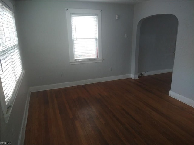 empty room with arched walkways, wood finished floors, and baseboards