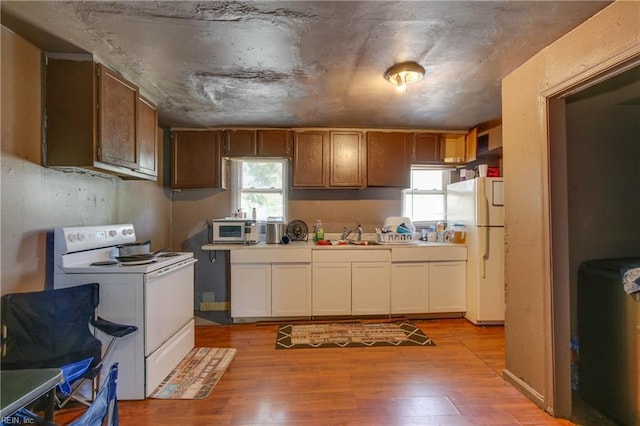 kitchen featuring white appliances, brown cabinetry, light countertops, light wood-style floors, and a sink