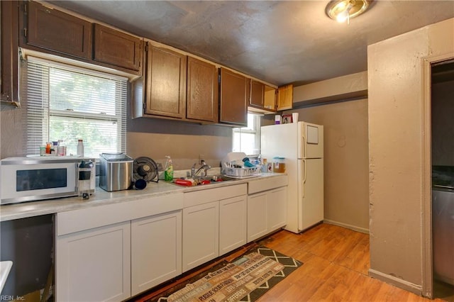 kitchen featuring light wood finished floors, light countertops, white appliances, and a sink