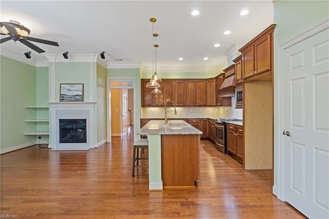 kitchen featuring brown cabinets, crown molding, appliances with stainless steel finishes, a sink, and premium range hood