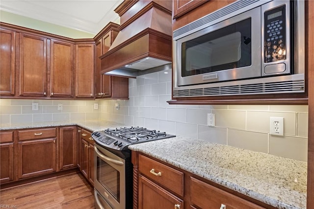 kitchen with appliances with stainless steel finishes, premium range hood, backsplash, and light stone countertops