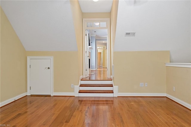 hallway with lofted ceiling, visible vents, baseboards, and wood finished floors