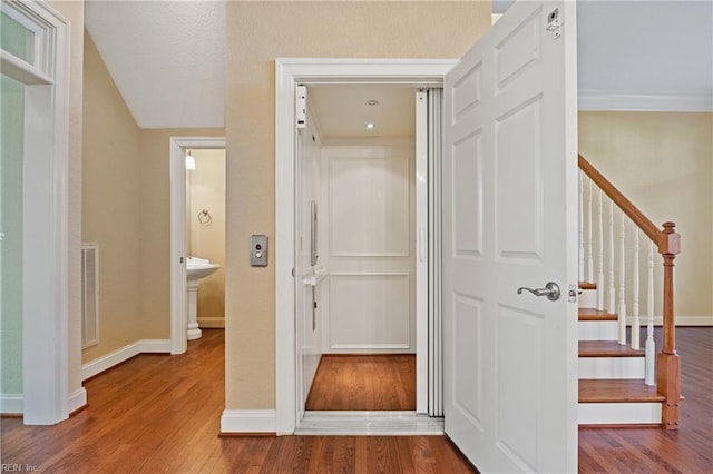 hallway featuring visible vents, elevator, wood finished floors, baseboards, and stairs