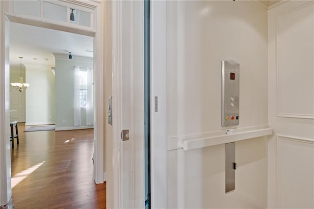 corridor with baseboards, ornamental molding, wood finished floors, and a notable chandelier