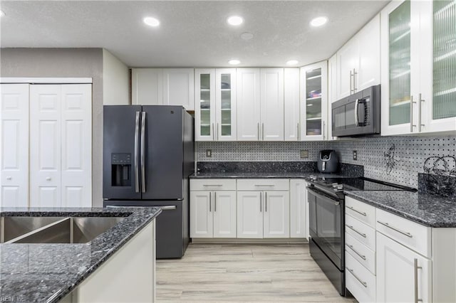 kitchen featuring light wood finished floors, tasteful backsplash, white cabinetry, dark stone countertops, and black appliances