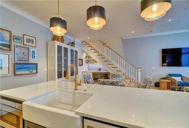 kitchen with crown molding, open floor plan, pendant lighting, light stone counters, and a sink